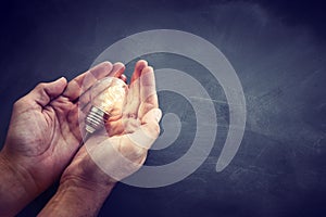 Education and business concept image. Creative idea and innovation. Man holding a light bulbs as metaphor over blackboard