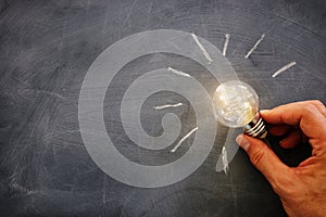 Education and business concept image. Creative idea and innovation. Man holding a light bulbs as metaphor over blackboard
