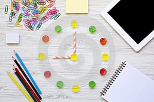 Education concept, back to school. Nine hours on watch. Clock made of colorful sweet candies, accessories for study over white woo