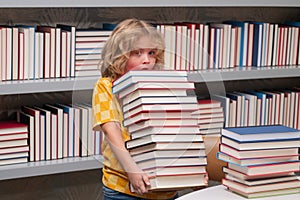 Education Concept. Little student boy reading book at school. Kid doing homework, sitting at table by books, in library.