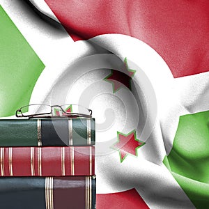 Education concept - Stack of books and reading glasses against National flag of Burundi
