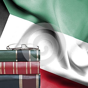 Education concept - Stack of books and reading glasses against National flag of Kuwait