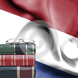 Education concept - Stack of books and reading glasses against National flag of Netherlands