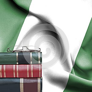 Education concept - Stack of books and reading glasses against National flag of Nigeria