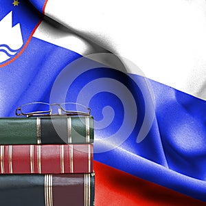 Education concept - Stack of books and reading glasses against National flag of Slovenia