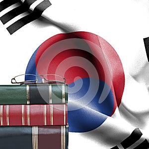 Education concept - Stack of books and reading glasses against National flag of South Korea