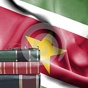 Education concept - Stack of books and reading glasses against National flag of Suriname