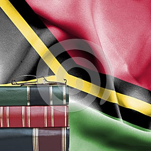 Education concept - Stack of books and reading glasses against National flag of Vanuatu