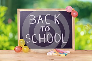 education concept with text back to school is written in chalkboard, colorful chalks and balloons on wooden table over green