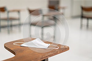 Education during COVID-19: A used medical facemask hangs on a wood lecture chair in empty classroom during COVID-19 pandemic