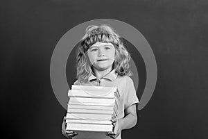 Education and creativity concept. Child holding stack of books with mortar board on blackboard. Back to school