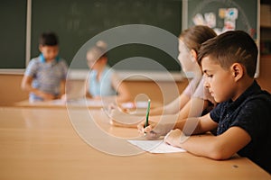 Education, elementary school. Learning and people concept - group of school kids with pens and notebooks writing test in