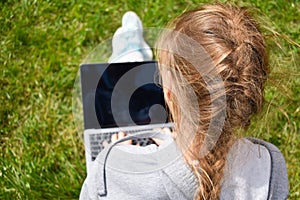 Education on the Internet. Teenager with laptop on grass. Girl freelancer