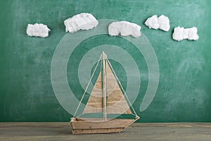 Education is a journey concept, toy boat under cotton clouds on the chalkboard background, inspiration for a fairy tale