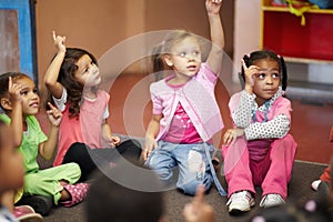 Education, kindergarten and kids asking a question with hands raised while sitting on a classroom floor for child