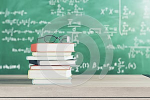 Education, learning and back to school concept with eyeglasses on stack of books on wooden table surface and blackboard with