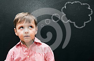 Education makes dream a reality. A young boy standing in front of a blackboard with a thought bubble drawn on it.