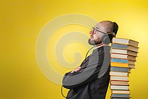 Education and modern technologies. The concept of audio books. A man in glasses, shirt, and earphones leaned against stack of