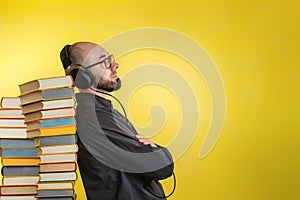 Education and modern technologies. The concept of audio books. A man in glasses, shirt, and earphones leaned against stacks of