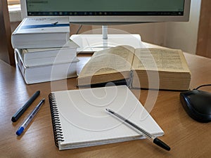 Education and online learning concept. Books, a notebook, pens and a computer mouse are on the table in front of the monitor.