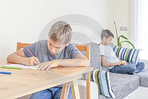 Education, online learning, distance learning, entertiment at home. Boy drawing with colored pencils. Brother using photo