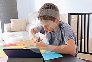 Education, paper crafts for kids. Child cutting colored paper with scissors. Boy looking video tutorial and making paper