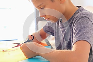 Education, paper crafts for kids. Child cutting colored paper with scissors and making greeting card at home