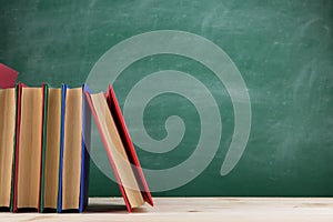 Education and reading concept - group of colorful books on the wooden table in the classroom, blackboard background