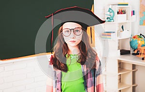 Education and school concept - little student girl studying at school. Portrait of cute schoolgirl with graduation hat