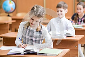 Education, school, learning and children concept - group of school kids with pens and textbooks writing test in classroom