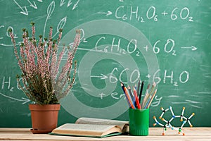 Education and sciences concept - bookand molecule model on the desk in the auditorium, photosynthesis formulas on the background