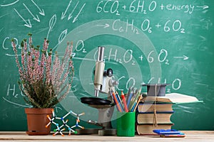 Education and sciences concept - books, molecule model and microscope on the desk in the auditorium, chalkboard background