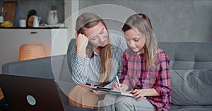 Education on self isolation period. Happy beautiful young Caucasian mother helping teenage daughter study on quarantine.