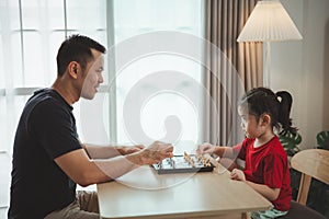 Education studying concept. Little cute asian baby girl children playing chess with her father dad in the living room at home.