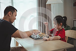 Education studying concept. Little cute asian baby girl children playing chess with her father dad in the living room at home.