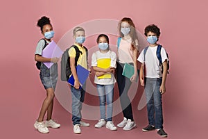 Education during virus outbreak. Diverse children with schoolbags and notebooks wearing masks on pink background