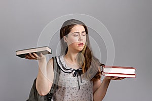 Education. A young woman or teenager with a backpack on her back, holding books in her hands, and looking at a large stack