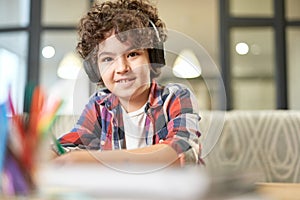 Education your way. Portrait of cheerful hispanic school boy wearing headphones, smiling at camera while preparing