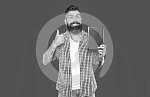 educational concept. cheerful bearded man recommend book on grey background, thumb up