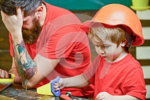 Educational games concept. Boy, child busy in protective helmet learning to use handsaw with dad. Father, parent with