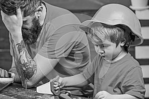 Educational games concept. Boy, child busy in protective helmet learning to use handsaw with dad. Father, parent with