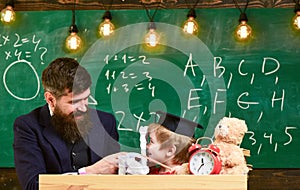 Educational games concept. Teacher with beard, father teaches little son in classroom, chalkboard on background. Boy