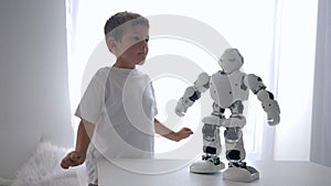 Educational toys, cute little boy repeats movements of robot with artificial intelligence close-up in room