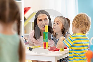 Educator helping kids playing with constructor in kindergarten photo