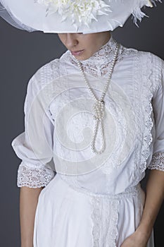 An Edwardian woman wearing a white lace blouse and skirt and a pearl necklace