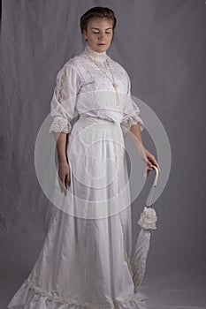 Edwardian woman in white blouse, skirt and hat standing against a studio backdrop