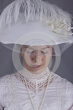 Edwardian woman in white blouse, skirt and hat standing against a studio backdrop