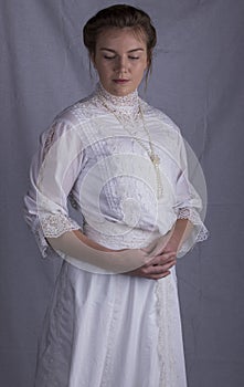 Edwardian woman in white blouse and skirt standing against a studio backdrop