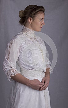 Edwardian woman in white blouse and skirt standing against a studio backdrop