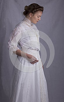 Edwardian woman in white blouse and skirt standing against a studio backdrop
